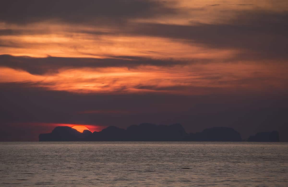 Backpacking Koh Lanta: TOP Things To Do & Itinerary 2025 6 watching an orange sunset fall behind a far away island in the ocean from koh lanta