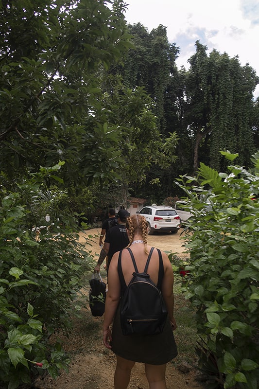 Rarru Cascades In Port Vila: BEST Tips For Visiting 2025 7 a women in braids and a black dress walking through some bushes at the car park in rarru cascades