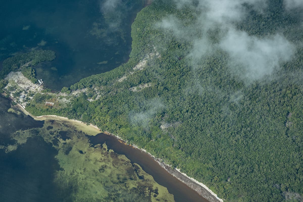Roatan To Belize: The BEST Scenic Commercial Flight 16 looking down on small buildings and jungle on a large island in belize