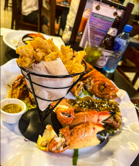 Best Restaurants In San Pedro Belize For Breakfast, Lunch & Dinner 12 An enticing seafood platter at Caramba Restaurant in San Pedro Belize, showcasing golden fried calamari in a paper-lined cone, with a whole grilled snapper and crab claws adorned in a savory sauce, perfect for food enthusiasts exploring the best places to eat in the vibrant town.