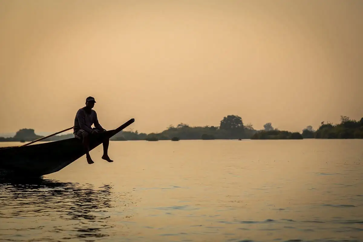 2 Weeks In Laos Itinerary: BEST Route North To South 50 a man sitting on the front of a boat in don det during sunset