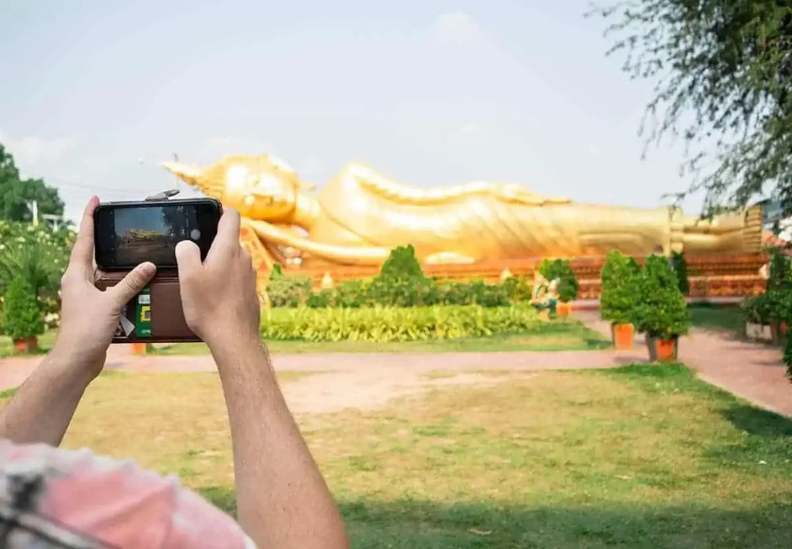 2 Weeks In Laos Itinerary: BEST Route North To South 29 a person taking a photo of his phone of the golden reclining buddha in vientiane