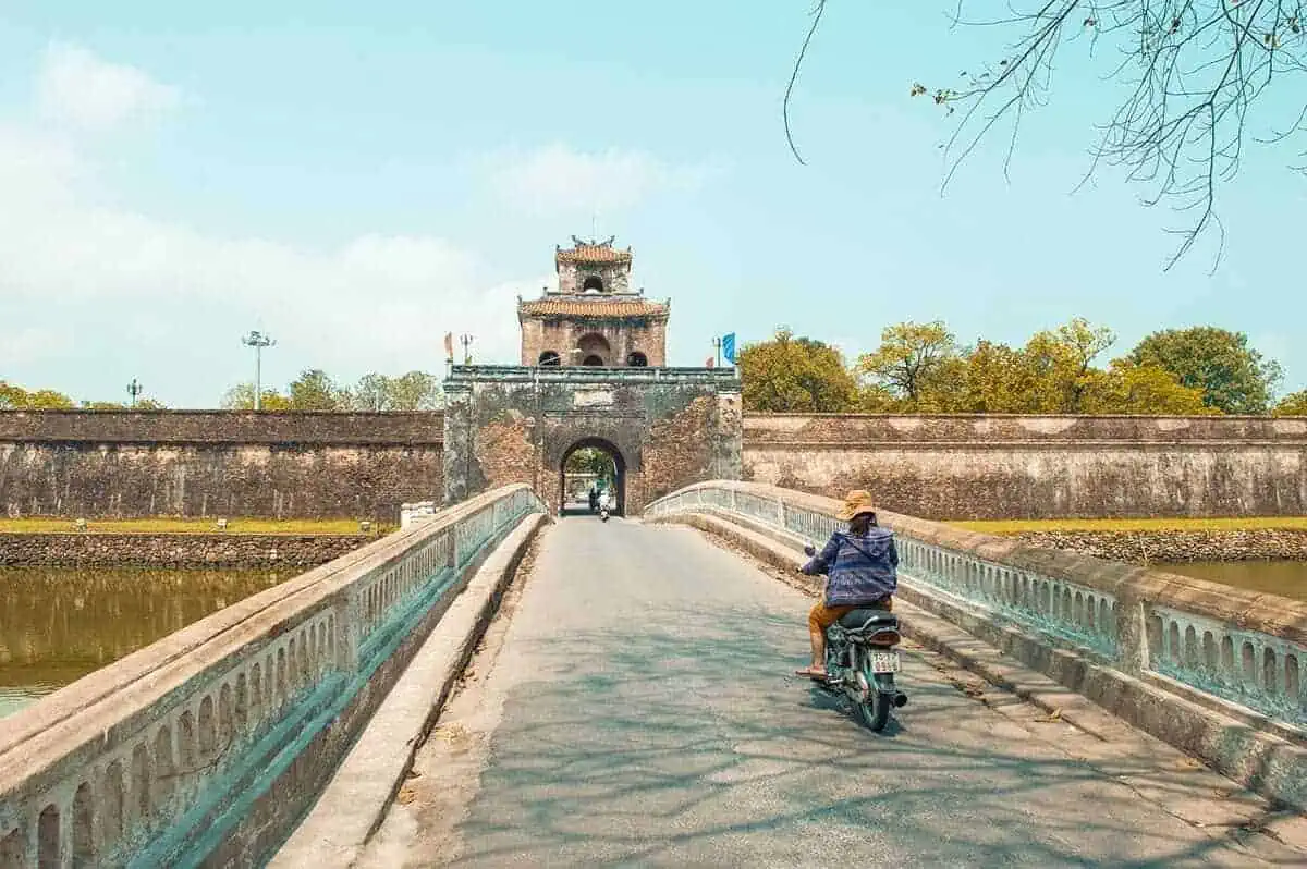 3 Week Vietnam Itinerary: BEST North To South Route 27 Motorcyclist crossing an ancient bridge leading to a historic gate in Hue, a cultural highlight for 3 weeks in Vietnam.