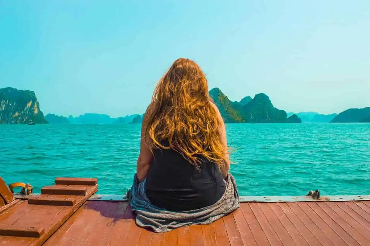 3 Week Vietnam Itinerary: BEST North To South Route 18 Woman sitting on a boat deck, admiring limestone cliffs emerging from the sea, a peaceful moment to savor on a 3 weeks in Vietnam journey.