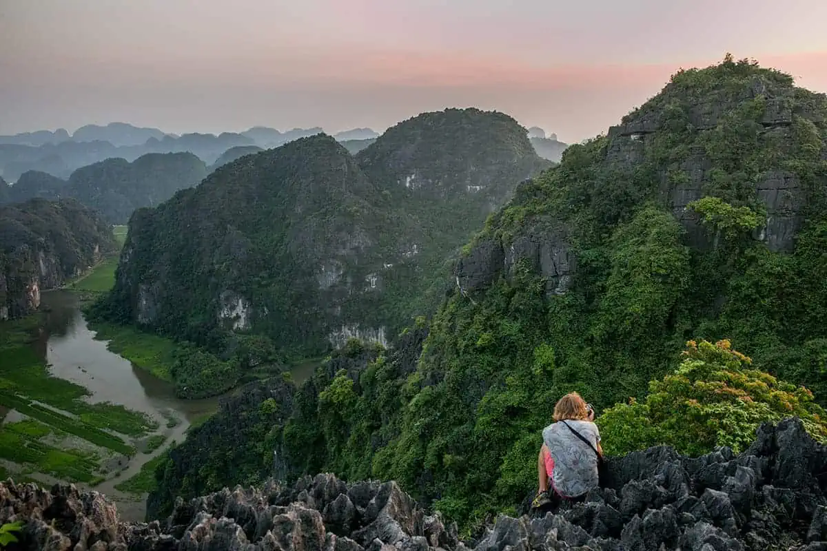 3 Week Vietnam Itinerary: BEST North To South Route 8 A traveler sitting atop rugged karst peaks overlooking the river in a valley on the ultimate 3 weeks in Vietnam itinerary