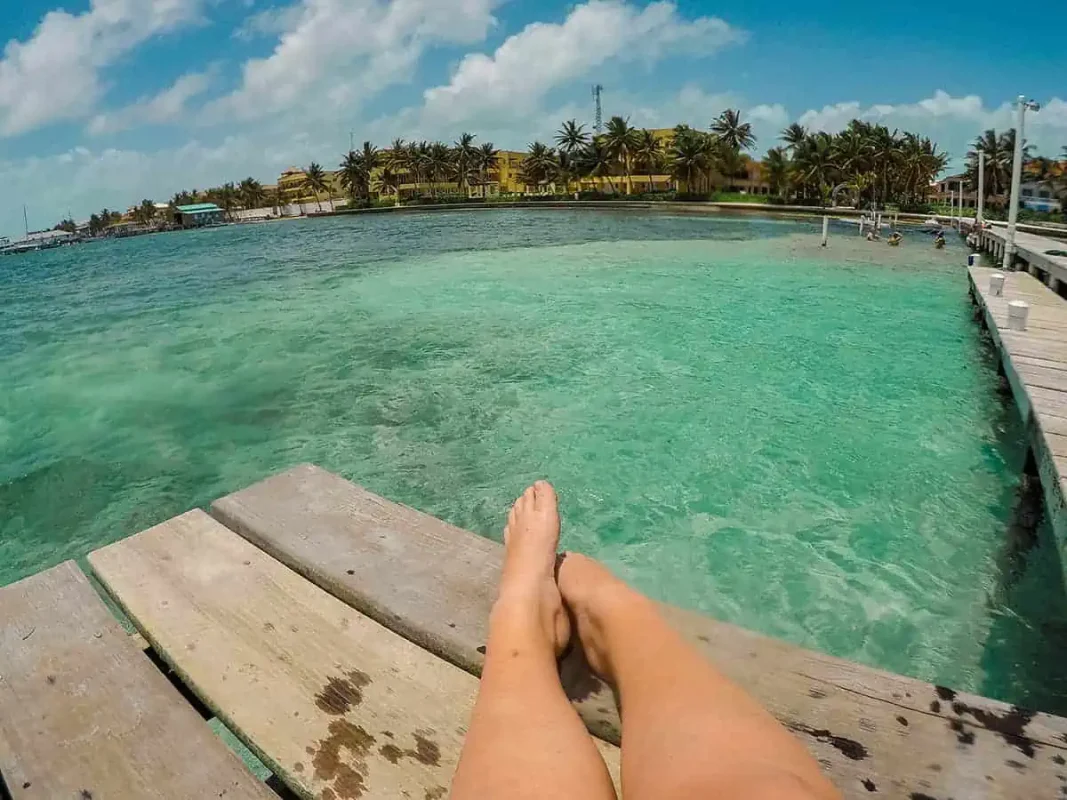 Ambergris Caye VS Caye Caulker: Which Island Is Best For Your Belize Paradise 4 Tasha Amys legs seen from a dock overlooking the clear waters of Ambergris Caye with a view of the tropical shoreline.