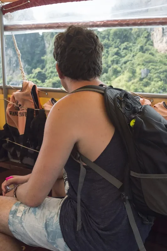 Ao Nang To Railay Beach: The ULTIMATE Guide 2025 7 A man with a backpack sitting on a longtail boat looking out at the cliffs during the journey to Railay Beach.