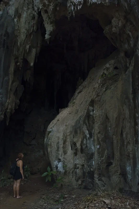 Ao Nang To Railay Beach: The ULTIMATE Guide 2025 8 tasha amy with a backpack standing at the entrance of a dark cave surrounded by limestone formations on Railay Beach.