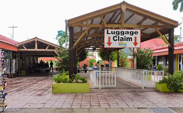 Bacalar To Caye Caulker: The ULTIMATE Travel Guide 2025 11 Small luggage claim area at the belize water taxi terminal. The area is surrounded by greenery and rustic buildings.