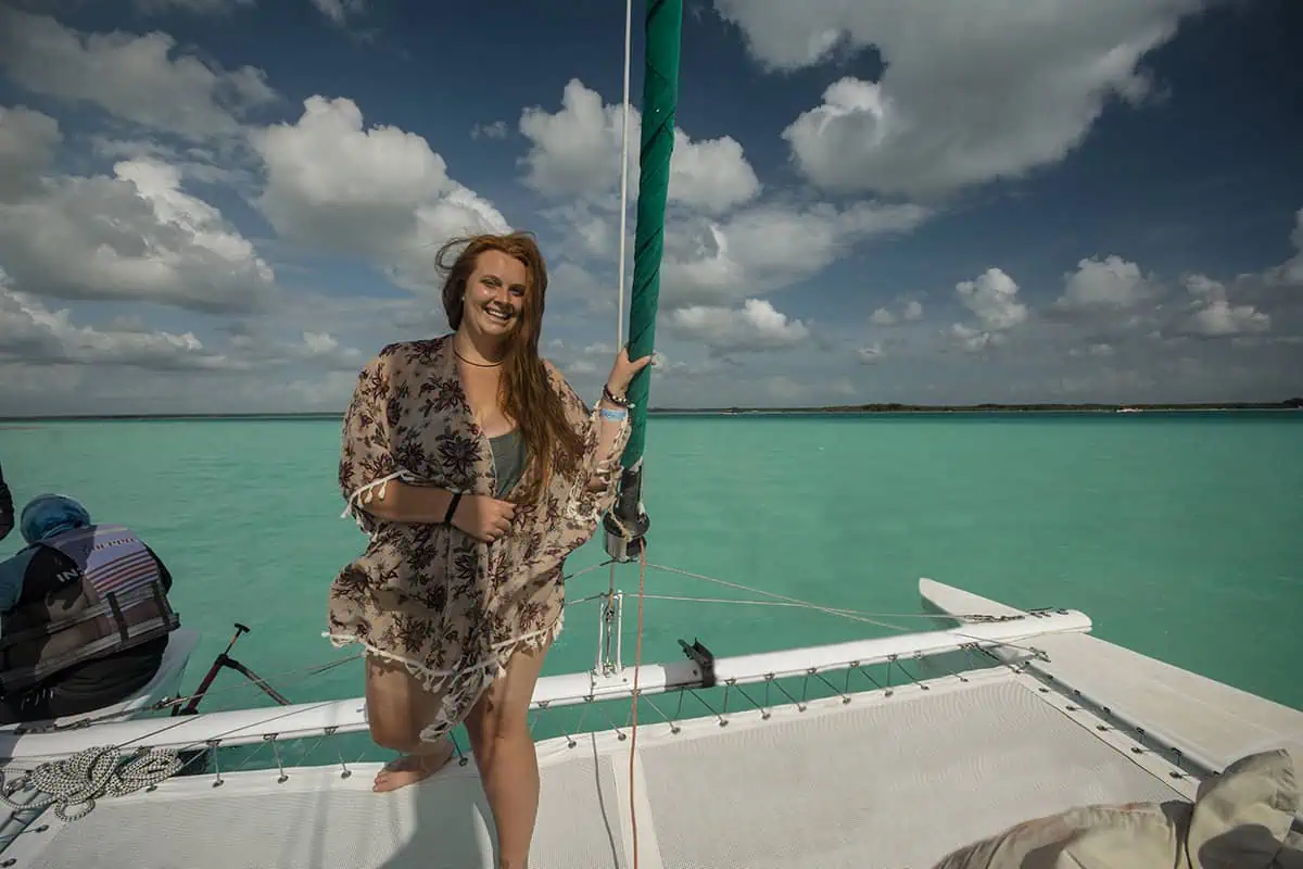 Bacalar To Caye Caulker: The ULTIMATE Travel Guide 2025 4 Tasha Amy stands on a sailboat in Bacalar Lagoon, wearing a kimono over her swimsuit. The water and sky create a picturesque backdrop.