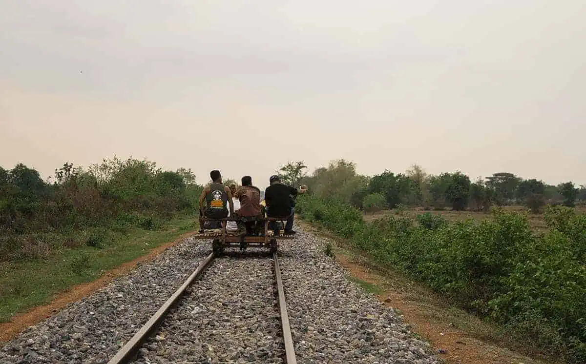 Battambang Bamboo Train: Is It Still Worth Visiting? 2025 25 A group of people riding a bamboo train cart along the railway, surrounded by vegetation and open countryside.