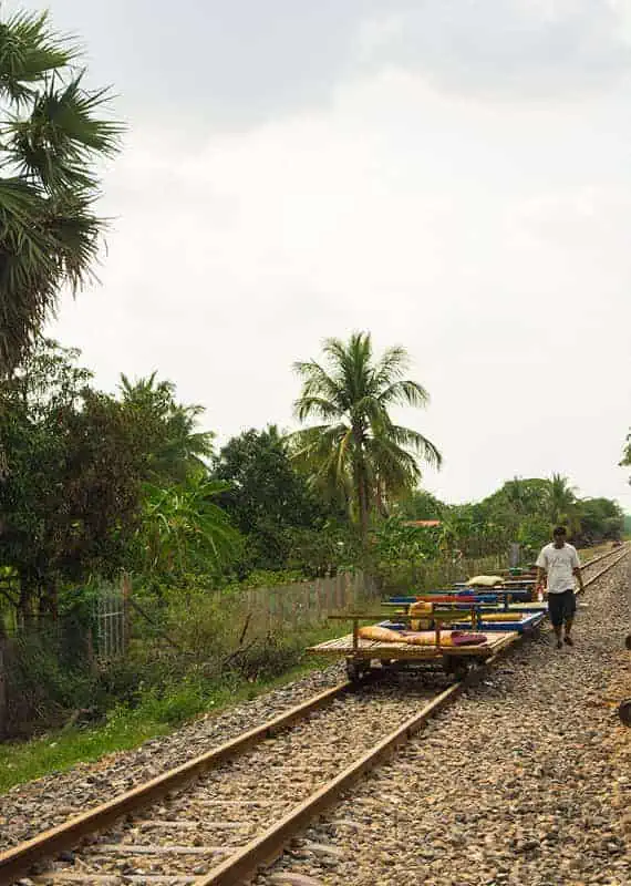 Battambang Bamboo Train: Is It Still Worth Visiting? 2025 17 A man walks alongside several bamboo train platforms lined up on an old railway track, setting them up for groups to jump on.