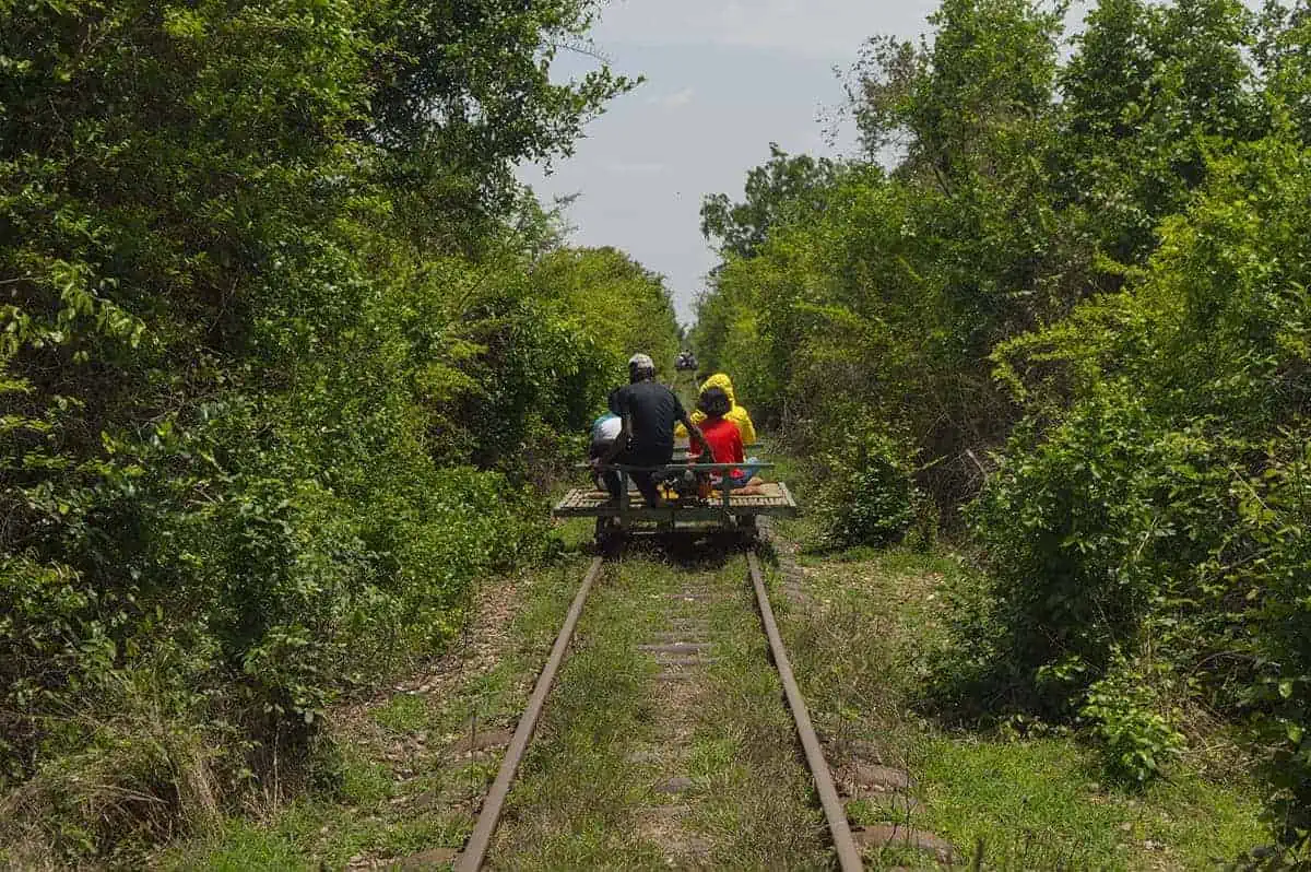 Battambang Bamboo Train: Is It Still Worth Visiting? 2025 10 the old bamboo train in 2017 with the overgrown jungle and track. A group ride the a narrow track, with bush forming a tunnel around the rails.