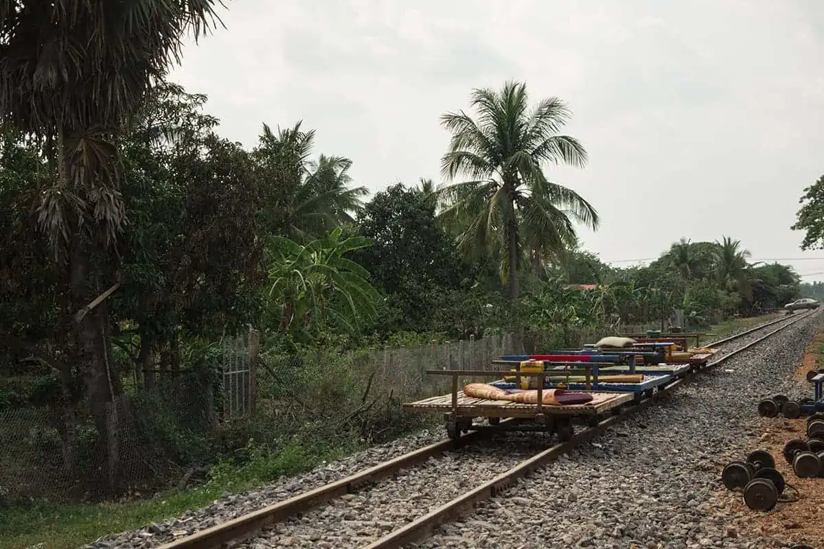 Battambang Bamboo Train: Is It Still Worth Visiting? 2025 11 Multiple bamboo trains rest on a railway line, with spare wheels on the ground.