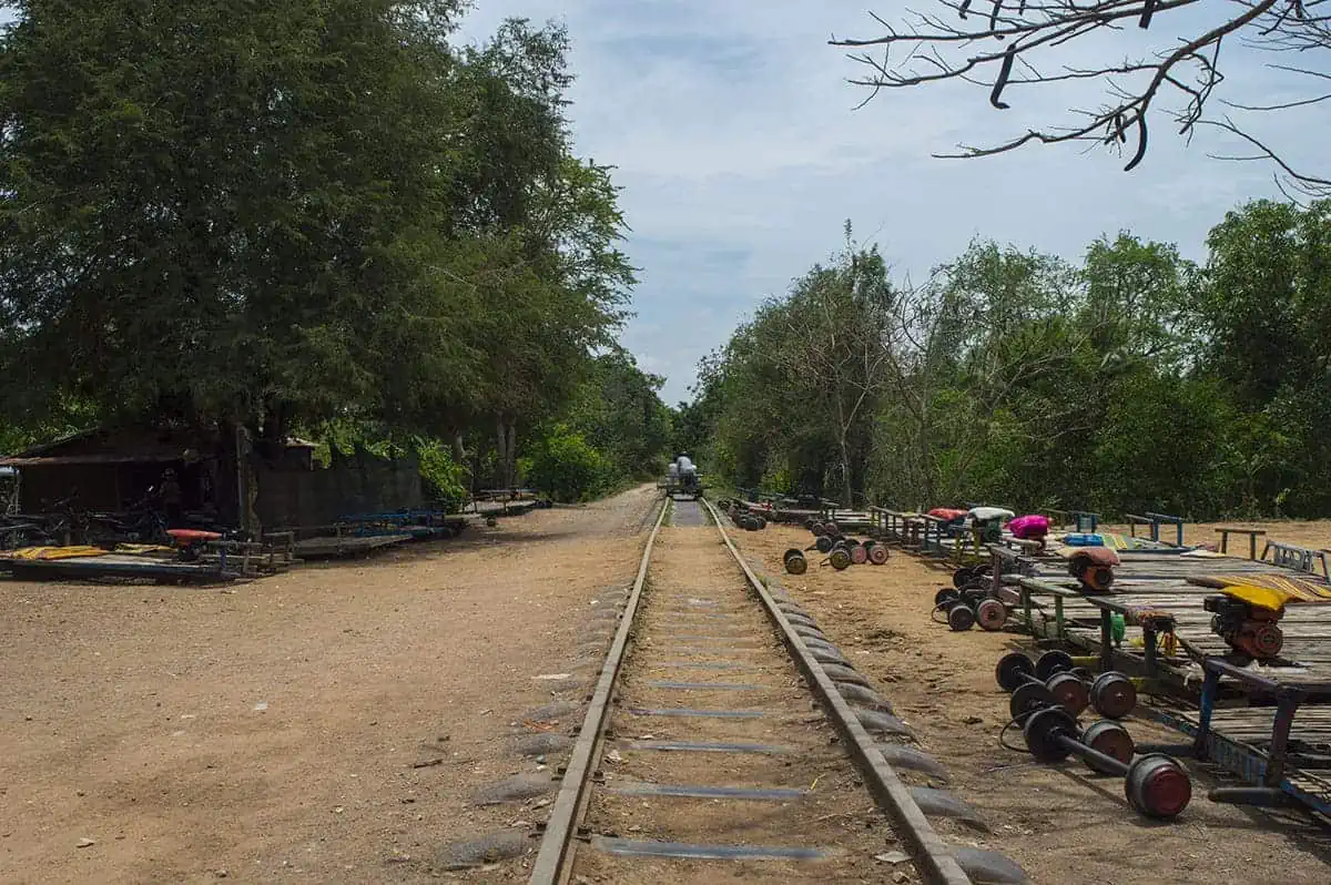 Battambang Bamboo Train: Is It Still Worth Visiting? 2025 1 A straight view down the Battambang bamboo train tracks, with rows of dismantled train carts and wheels resting on both sides of the rail line.