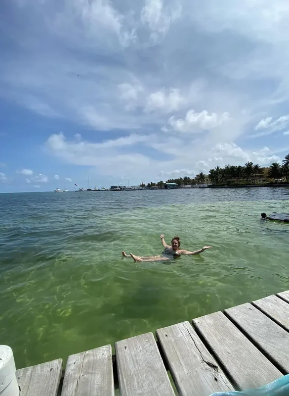Tasha Amy floating joyfully in the clear turquoise waters off a wooden dock in Belize, showcasing the leisure activities available in the sunny month of June.