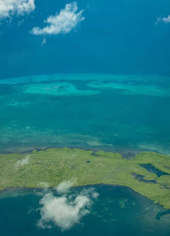 Aerial view of the Belize Barrier Reef with patches of coral and a small island, illustrating the stunning natural beauty accessible in June.