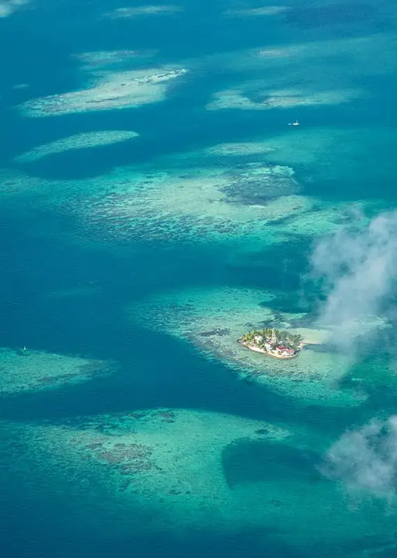 A small, picturesque island surrounded by the azure Caribbean Sea off the coast of Belize, seen from above in the clear weather of June.
