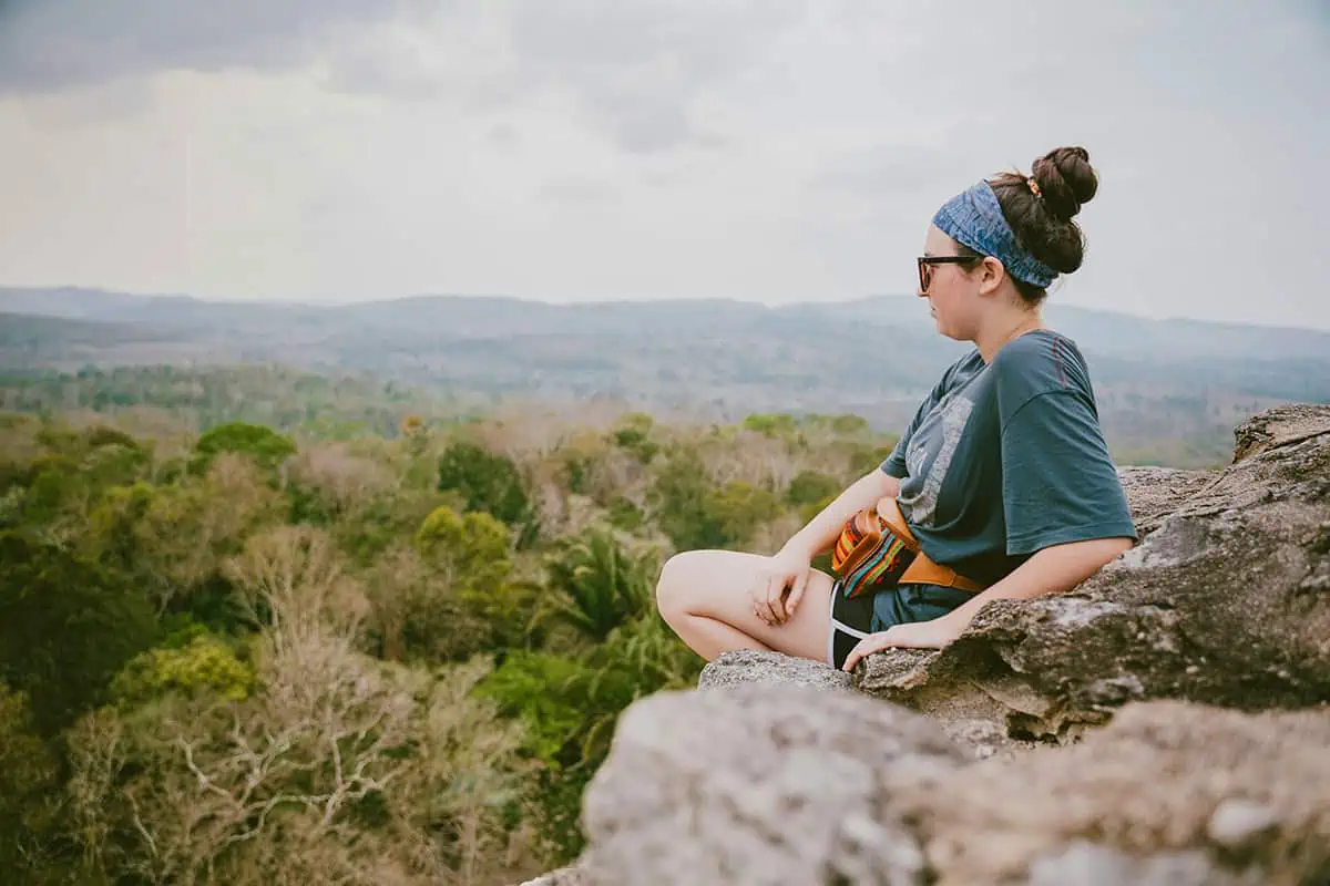 Ultimate Belize Puns & Captions For An Un-Belize-able Laugh 4 A serene moment captured as a person sits atop a rocky outcrop, gazing across the vast jungle landscape of Belize, perfect for reflective Belize Instagram captions and Belize puns
