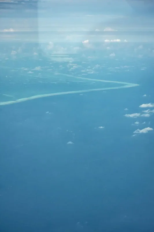 Aerial view of one of the atolls in Belize, showcasing the vast blue ocean with a narrow strip of the atoll visible, creating a serene and isolated scene.