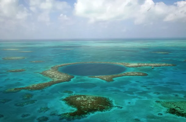 Aerial view of the famous Great Blue Hole at lighthouse atoll in Belize surrounded by shallow coral reefs and a solitary boat near its edge, illustrating the scale and beauty of this natural wonder.
