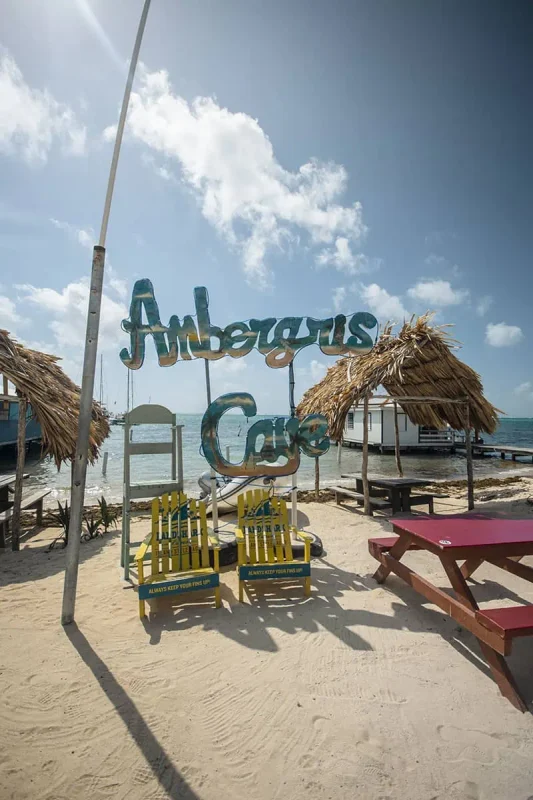 Best Beaches In Ambergris Caye: For Swimming, Snorkeling, Tanning & More 14 A vibrant sign reading "Ambergris Caye" with a picnic table and thatched structures in the background, depicting a popular spot for tourists to visit on the island.