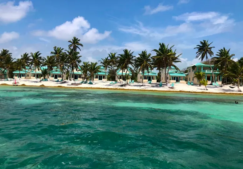 Best Beaches In Ambergris Caye: For Swimming, Snorkeling, Tanning & More 8 Vibrant aquamarine waters brushing against the white sandy beach of Ambergris Caye, lined with tropical palm trees and charming pastel-colored beachfront villas.