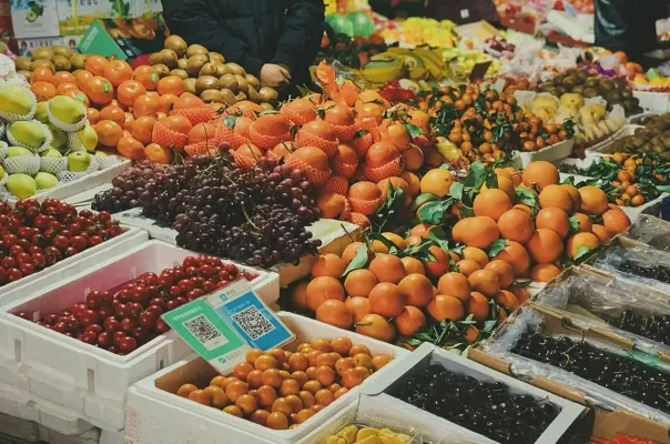 A vibrant array of fruits for sale at a market, featuring oranges, kiwis, grapes, and strawberries, showcasing the diversity of fruits in Belize.