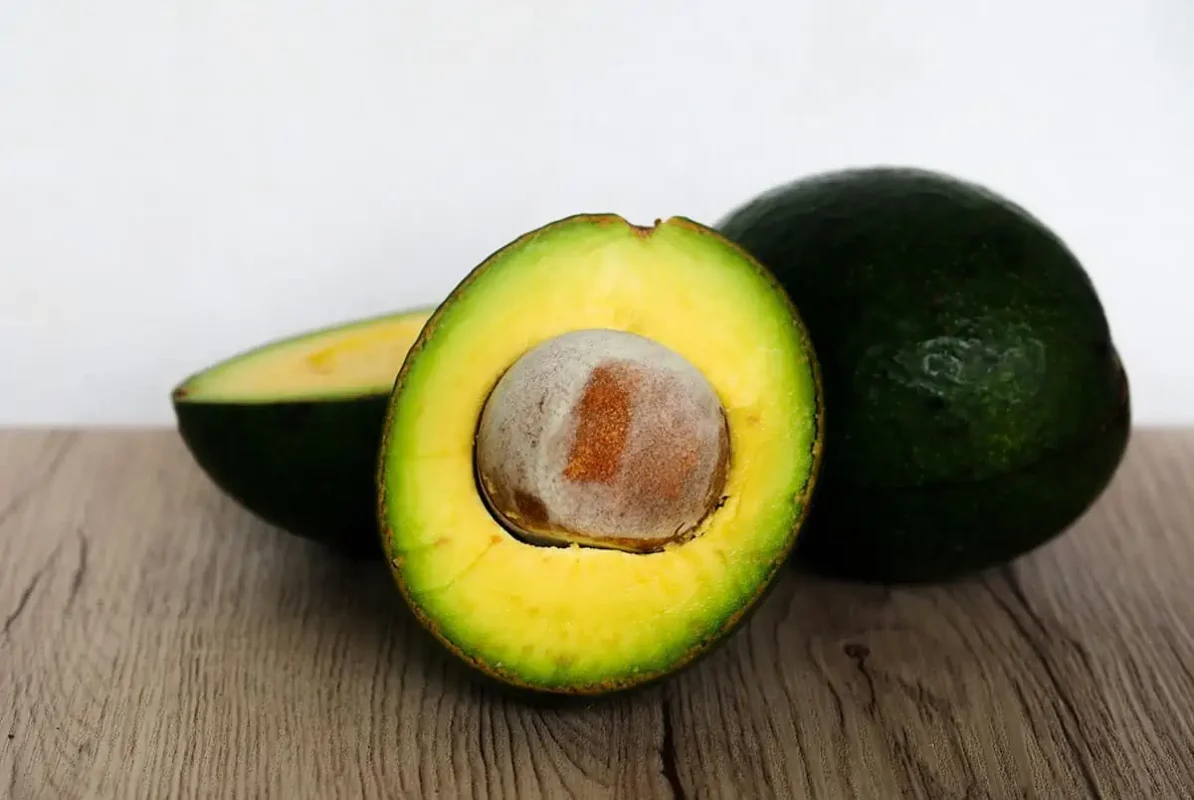 Fruits In Belize: The BEST 24 Fruits Worth Trying On Your Visit 18 A halved avocado with a rich, creamy texture and a large brown pit, presented on a wooden surface.