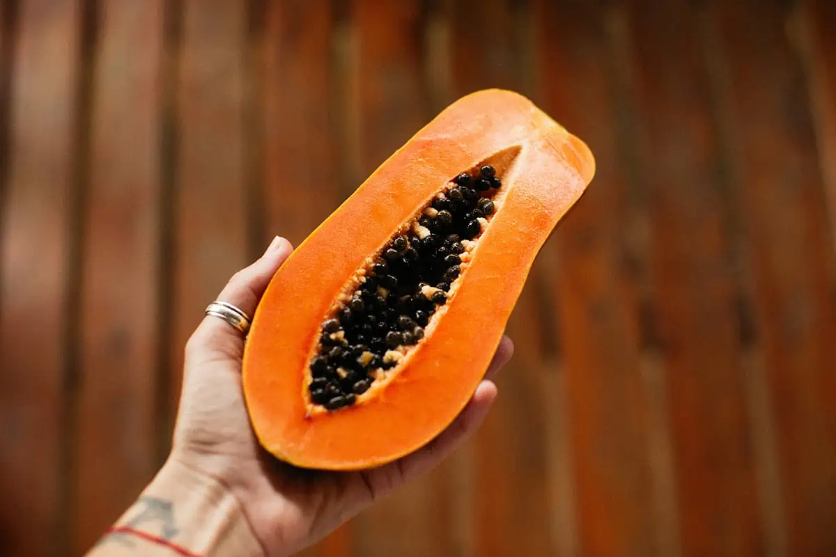 Fruits In Belize: The BEST 24 Fruits Worth Trying On Your Visit 6 Hand holding a half-cut ripe papaya with black seeds, highlighting the vibrant orange flesh of this tropical fruit found in Belize.