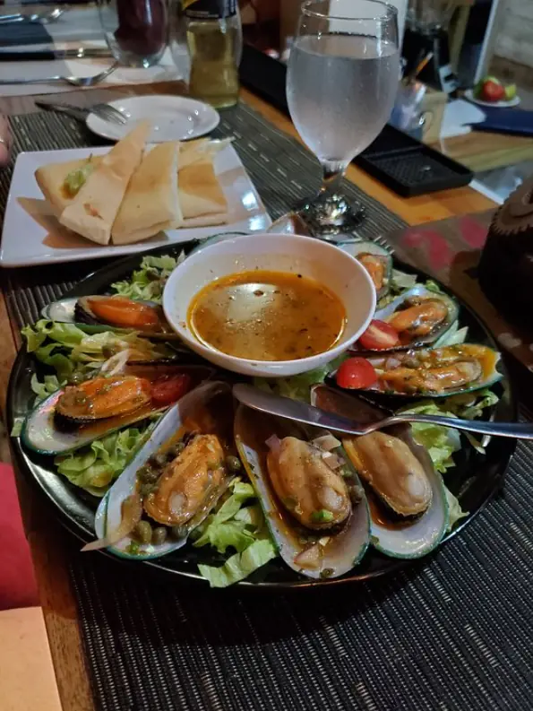 12 Best Restaurants In San Ignacio: Top Eats For Visitors 13 A tantalizing plate of mussels in a garlic broth with fresh greens and toasted bread on the side from crave house of flavors, a must-try dish in San Ignacio's dining scene.