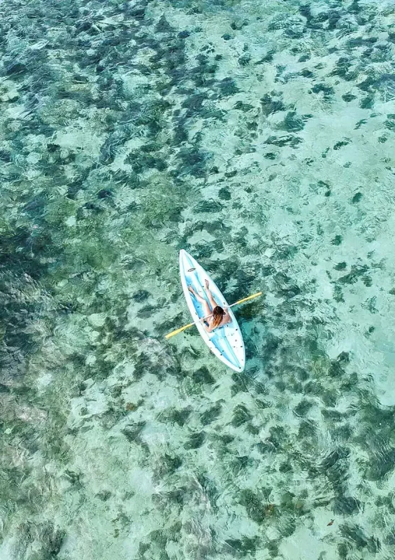 The 31 BEST Things To Do In Caye Caulker: Ultimate List! 12 Aerial view of a woman kayaking on the clear, shallow waters of Caye Caulker. The water's transparency reveals the seagrass below, creating a stunning mosaic of blues and greens. Kayaking is one of the best things to do in Caye Caulker, offering a peaceful way to explore the marine environment.