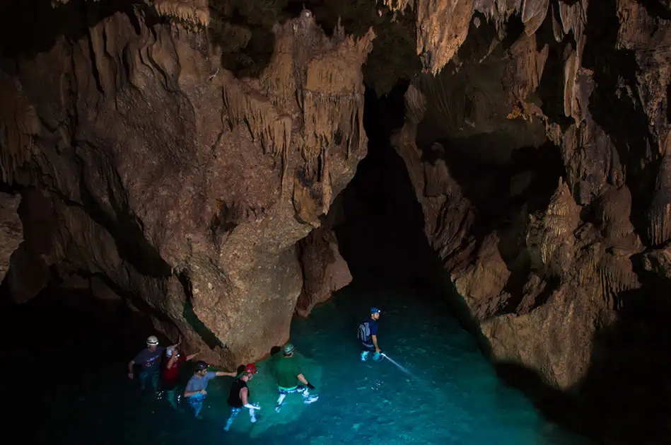 25+ Best Things To Do In San Ignacio, Belize (2025) 19 Group of people wading through crystal-clear water inside a dark, ATM cave. They are wearing helmets and headlamps, and the scene captures the sense of adventure and excitement, highlighting one of the thrilling things to do in San Ignacio.