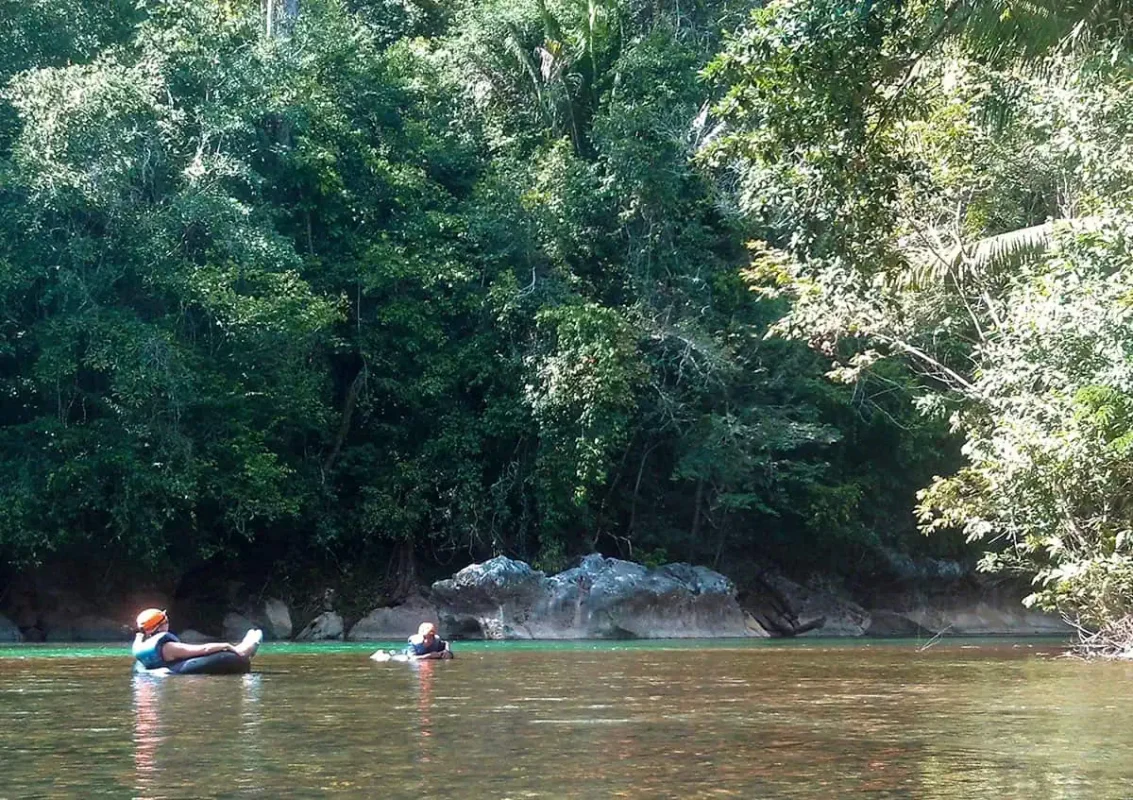 25+ Best Things To Do In San Ignacio, Belize (2025) 7 Two people floating on inner tubes in a calm river surrounded by dense jungle in San Ignacio. The participants are wearing life vests and helmets, enjoying the peaceful tubing experience as one of the adventurous things to do in San Ignacio.