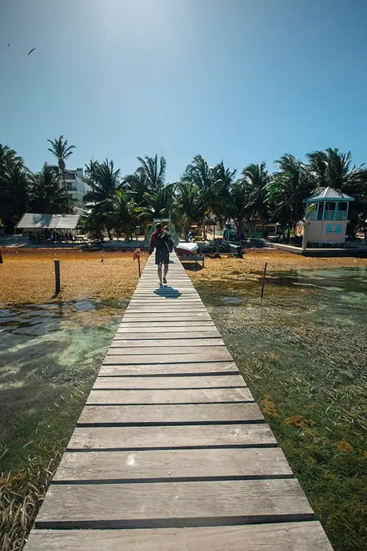 Caye Caulker To Belize City: Best & Easiest Ways 4 A person walking down a wooden pier near a beach in Caye Caulker.
