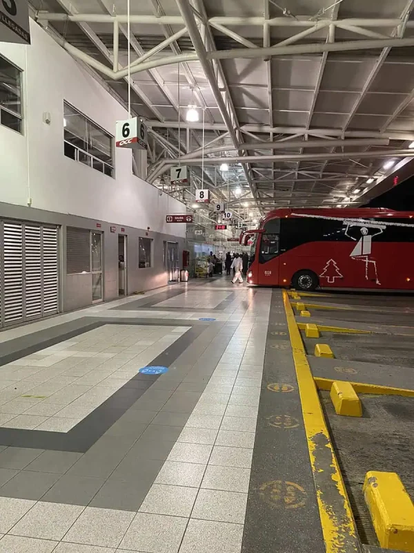 The interior of a bus terminal with designated bus bays and a red ADO bus parked at Bay 6. This is part of the journey from Chetumal to Caye Caulker, offering bus transportation before reaching the water taxi.