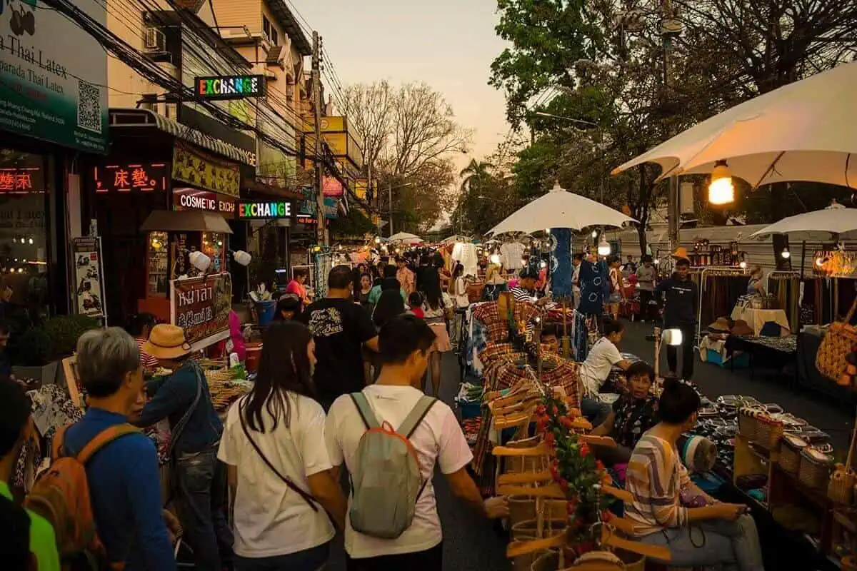 Chiang Mai Sunday Night Market: BEST Tips & Guide (2025) 9 Shoppers and vendors on a busy street with stalls offering a variety of goods during golden hour.