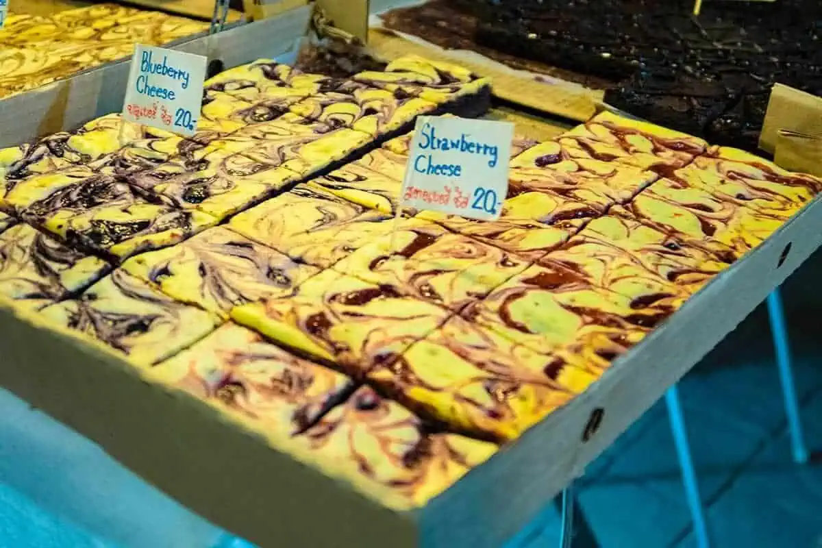 Chiang Mai Sunday Night Market: BEST Tips & Guide (2025) 25 Trays of blueberry and strawberry cheesecake bars attractively arranged for sale at the Sunday market in Chiang Mai.