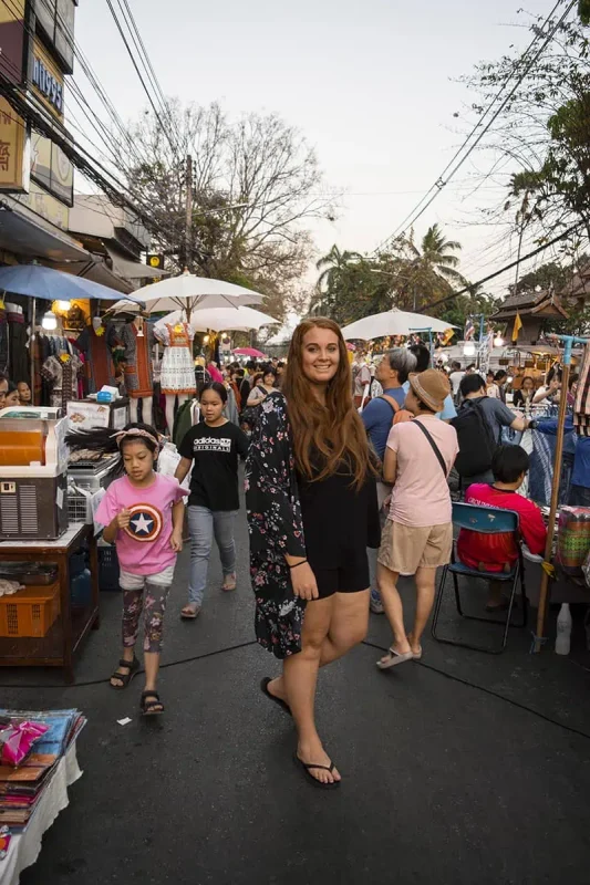 Chiang Mai Sunday Night Market: BEST Tips & Guide (2025) 12 Tasha Amy smiling as she navigates through the bustling lanes of the Sunday Market in Chiang Mai, surrounded by diverse market stalls.
