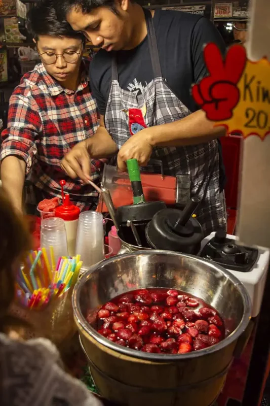 Chiang Mai Sunday Night Market: BEST Tips & Guide (2025) 15 Vendors preparing drinks at a stall with a colorful display of straws and a large bowl of strawberries.