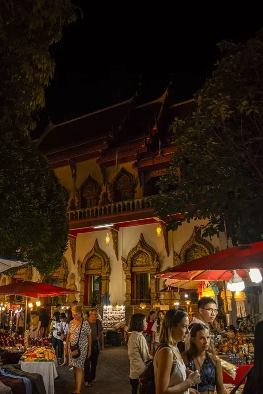 Chiang Mai Sunday Night Market: BEST Tips & Guide (2025) 21 A serene night scene at a temple, with market stalls and visitors around it in Chiang Mai at the market