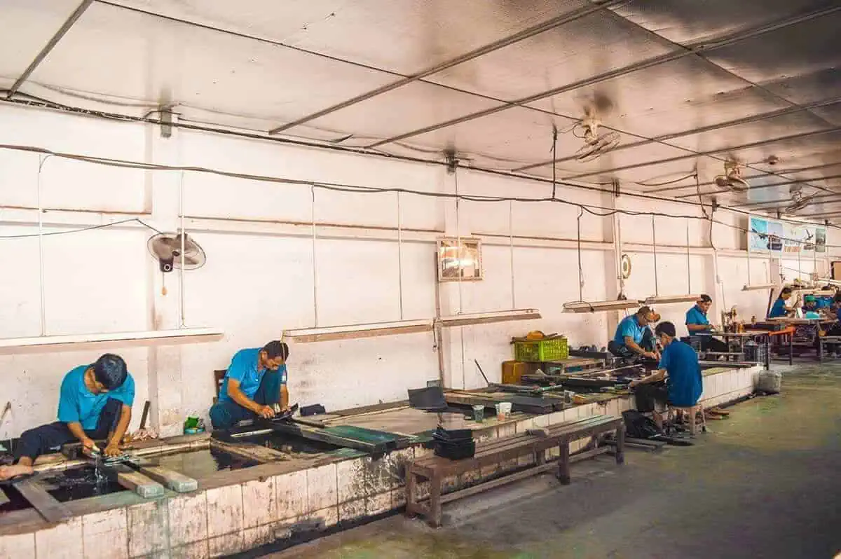 Best Cu Chi Tunnels Tours: Cheap VS Expensive 2025 5 Workers in blue uniforms at the lacquer stop off during the cu chi tunnels tour demonstrating manufacturing processes.