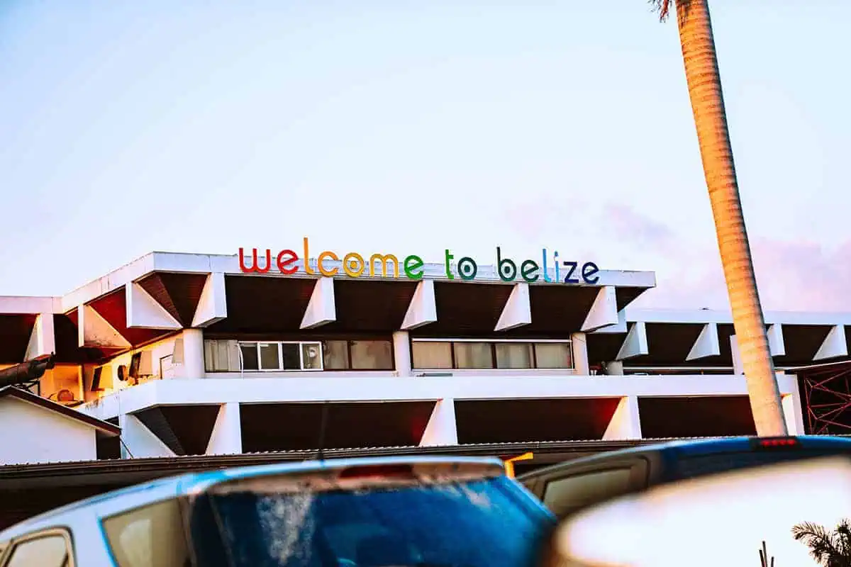 Flores To Belize City: Bus, Shuttle, Or Flight? (2025) 8 A welcoming sign at an airport in Belize City reads "welcome to belize" in colorful letters. The modern architecture of the airport terminal is partially visible, highlighting the end of the journey from Flores to Belize City.