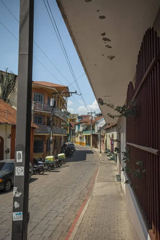 Flores To Belize City: Bus, Shuttle, Or Flight? (2025) 12 A narrow street in Flores, showcasing tightly packed houses with balconies and motorbikes parked along the sides. This scene represents the bustling yet charming streets of Flores.