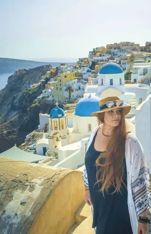 22+ Cheapest Countries To Backpack In The World! (2025) 31 A woman in a hat standing in front of a village in santorini.