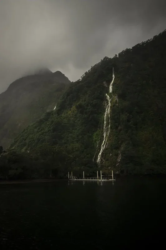 Is Milford Sound Worth It? My Pros & Cons 6 A tall and narrow waterfall running down steep cliffs into the waters of Milford Sound.