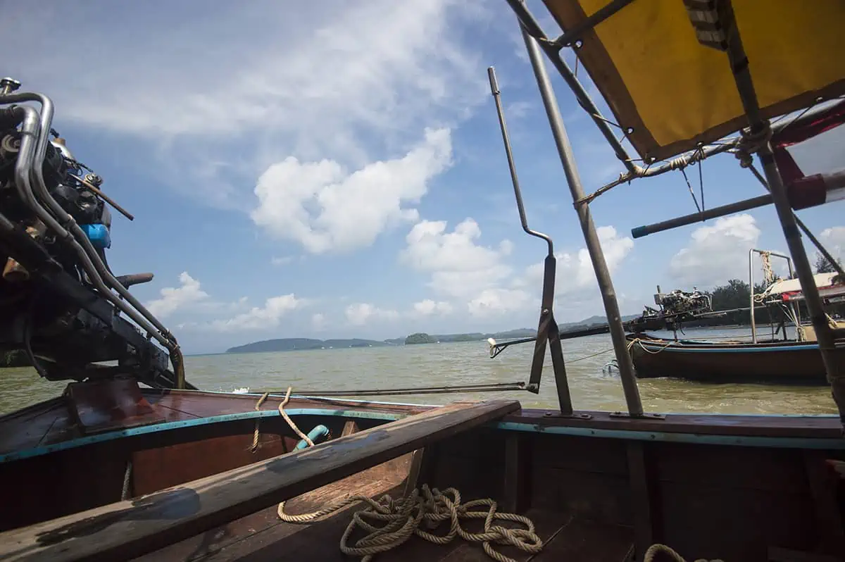 Is Railay Beach Closed: What You Need To Know (2025) 15 View from a long-tail boat on Railay Beach, showing the engine, a coiled rope, and the expansive sea under a bright blue sky with scattered clouds. This image suggests boating activities are ongoing, posing the question: "Is Railay Beach closed?"
