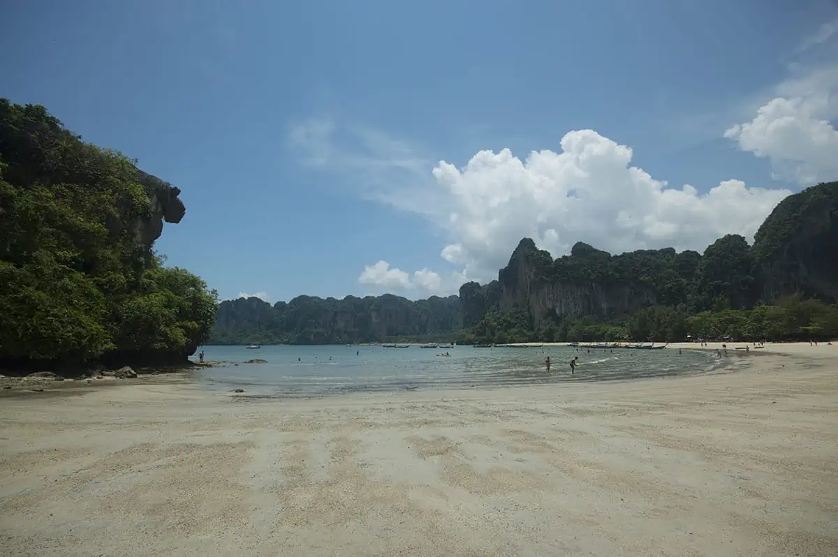 Is Railay Beach Closed: What You Need To Know (2025) 4 A wide view of Railay Beach with its iconic limestone cliffs in the background and a few people enjoying the shallow waters.