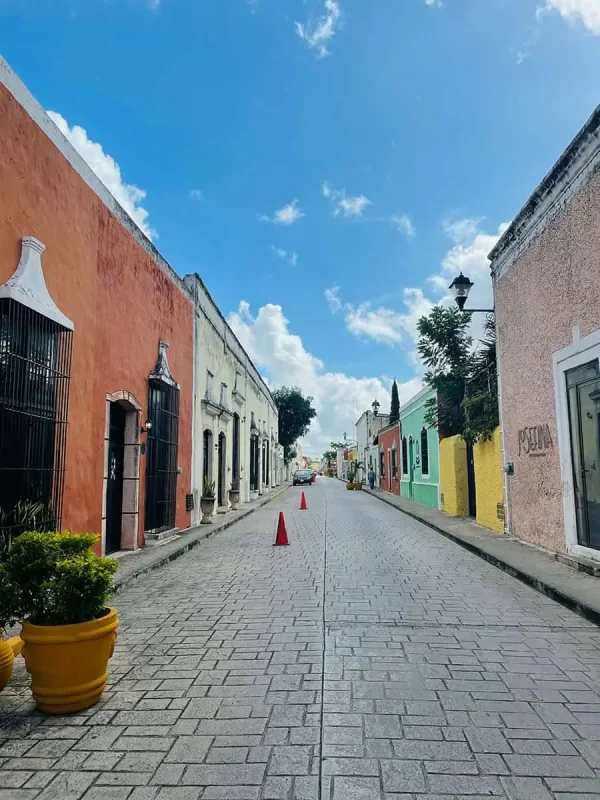 Charming street scene in Valladolid, with brightly painted buildings lining a cobblestone road under a clear blue sky. The vibrant facades and quaint atmosphere make it a delightful destination on a Mexico and Belize itinerary