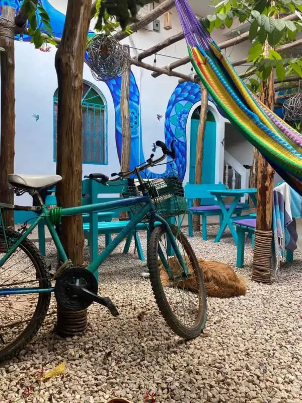 Mexico Belize Guatemala Itinerary: BEST Backpacking Route 51 A vibrant and artistic courtyard in Flores featuring a green bicycle parked on a gravel ground, colorful hammocks, and a large mural of a blue octopus on the wall. The scene is embellished with various hanging decorations and plants, creating a lively and welcoming atmosphere.